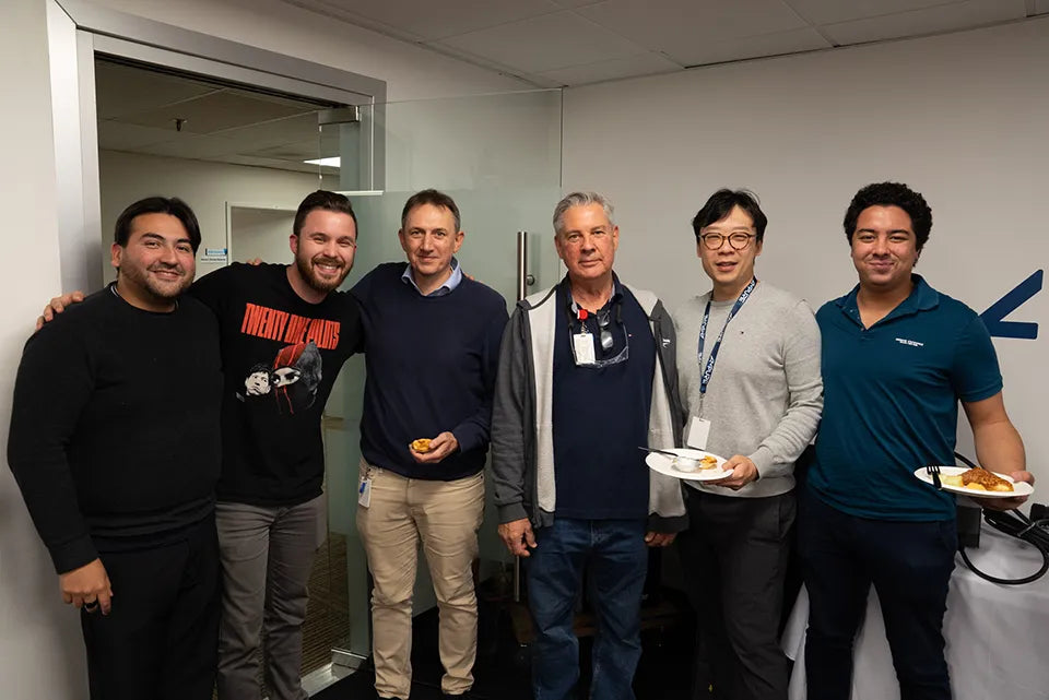 Group of six men posing together in an indoor setting, possibly an office or lab.