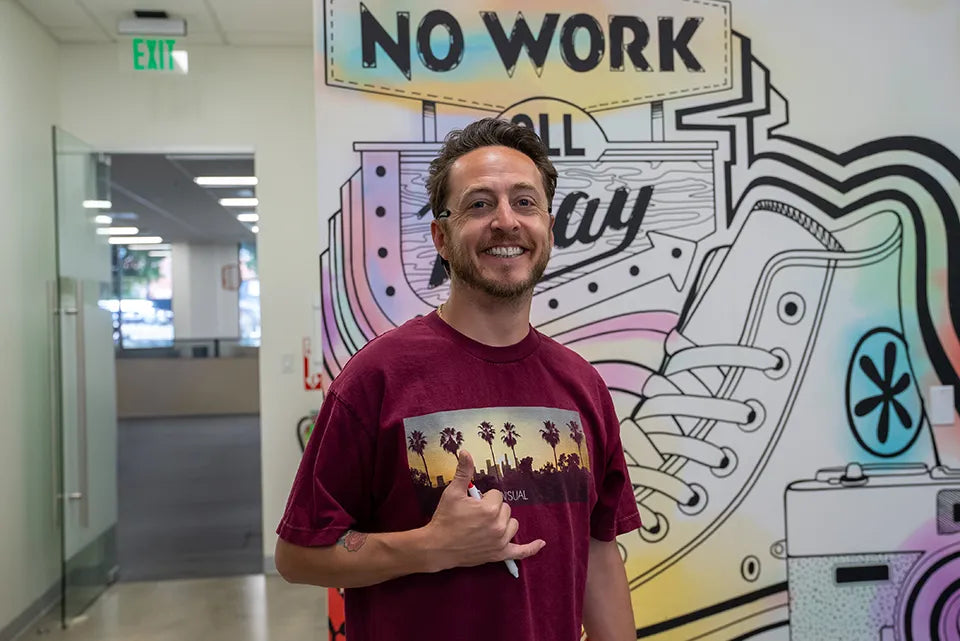 Man in maroon t-shirt with graphic design standing in front of colorful wall art with text