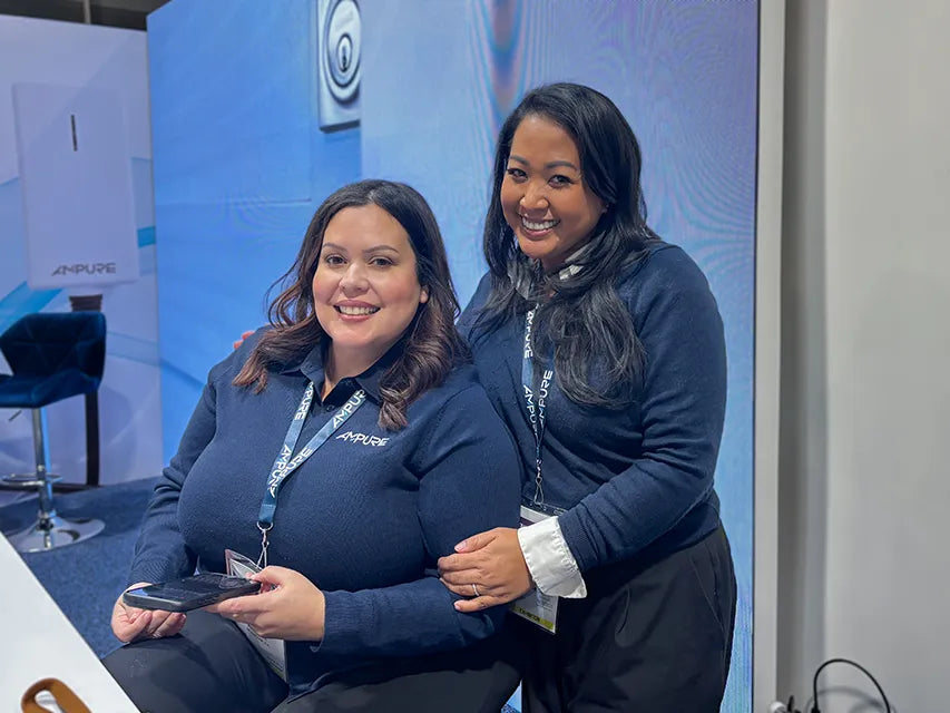 Two women in blue shirts with lanyards standing in front of a blue and white background